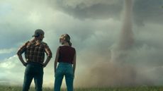 Glen Powell and Daisy Edgar-Jones facing away from the camera looking at a Tornado in "Twisters"