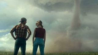 Glen Powell and Daisy Edgar-Jones facing away from the camera looking at a Tornado in "Twisters"