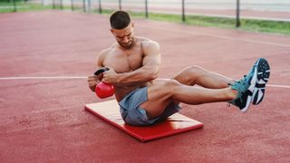 Man performing a Russian twist outdoors with a medicine ball