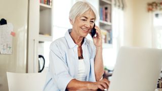 Elderly woman smiling on the phone while checking her laptop