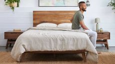 A man sits on the edge of an Avocado Green organic latex hybrid mattress in a bedroom, the mattress is dressed in Avocado bedding