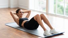 Woman in the gym performing a sit-up with hands behind head on exercise mat